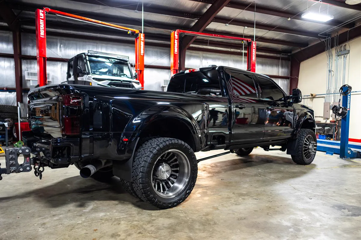 Lifted black Ford dually crew cab on forged wheels in the shop