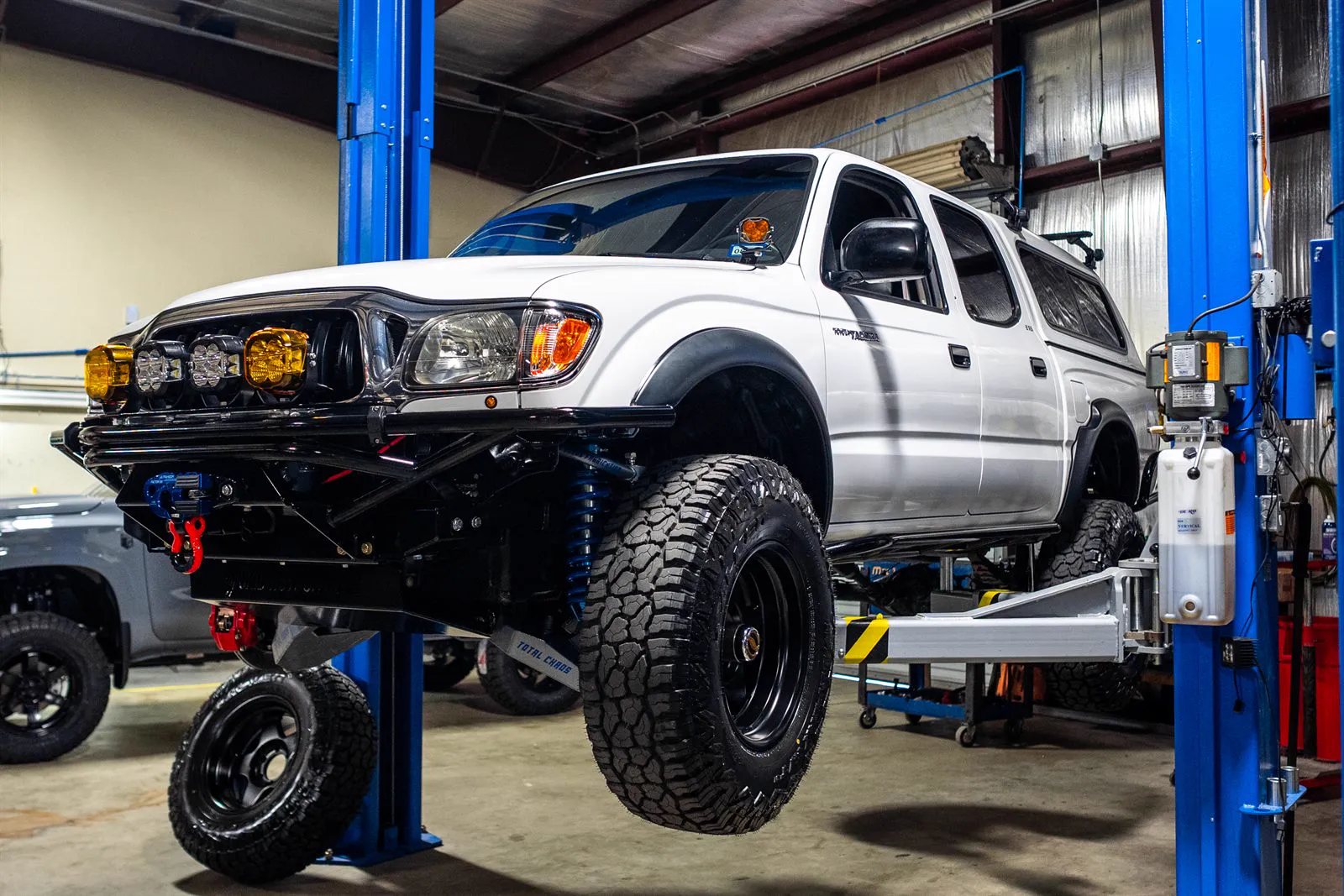 White Toyota Tacoma with long-travel suspension and light bar on the lift
